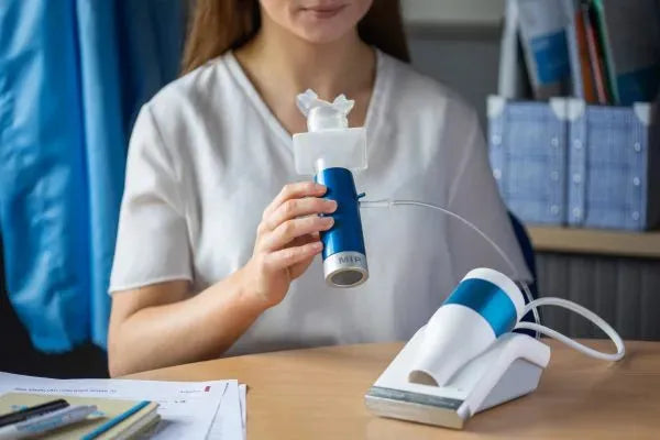 A woman seated at a desk is preparing to use the Pneumotrac™ with RMS (Respiratory Muscle Strength) system.